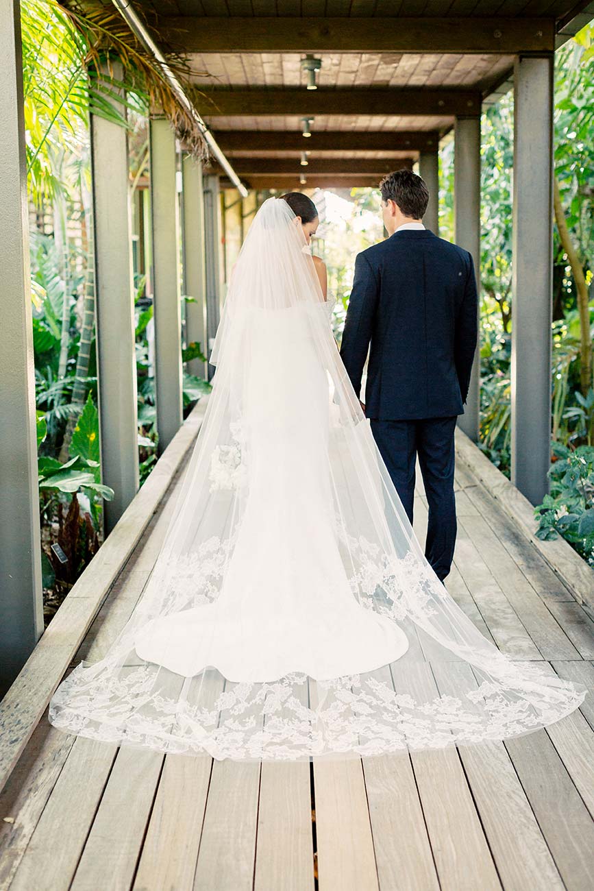 Bride and groom walking away from camera down outdoor hallway