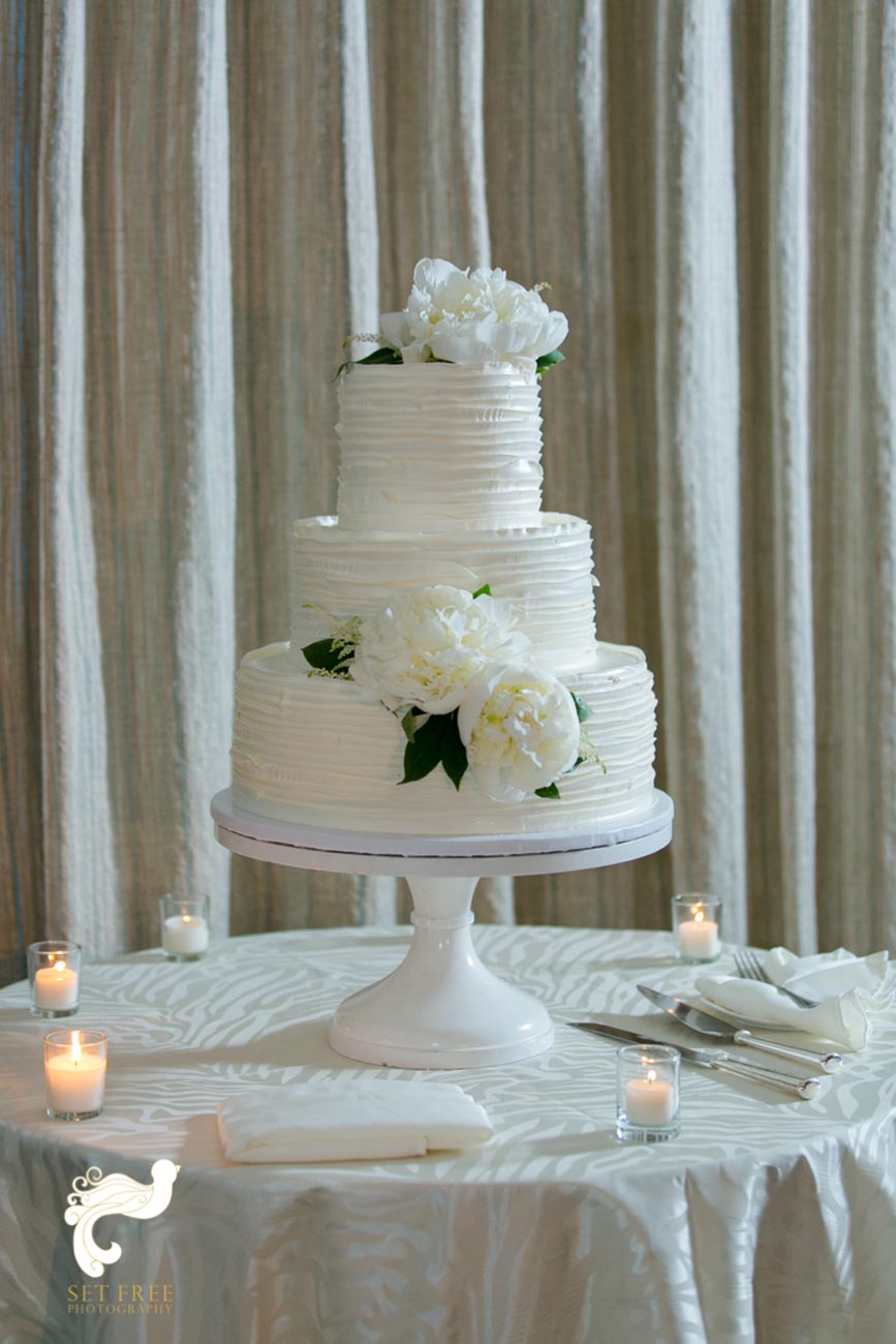 White three-tiered wedding cake on cake pedestal surrounded with tea lights