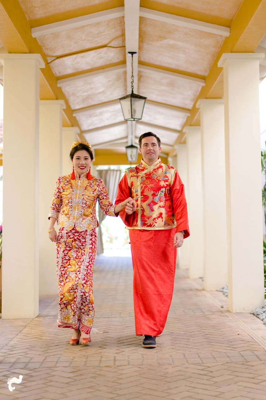 Bride and groom, in traditional Chinese wedding attire, walking down outside hallway