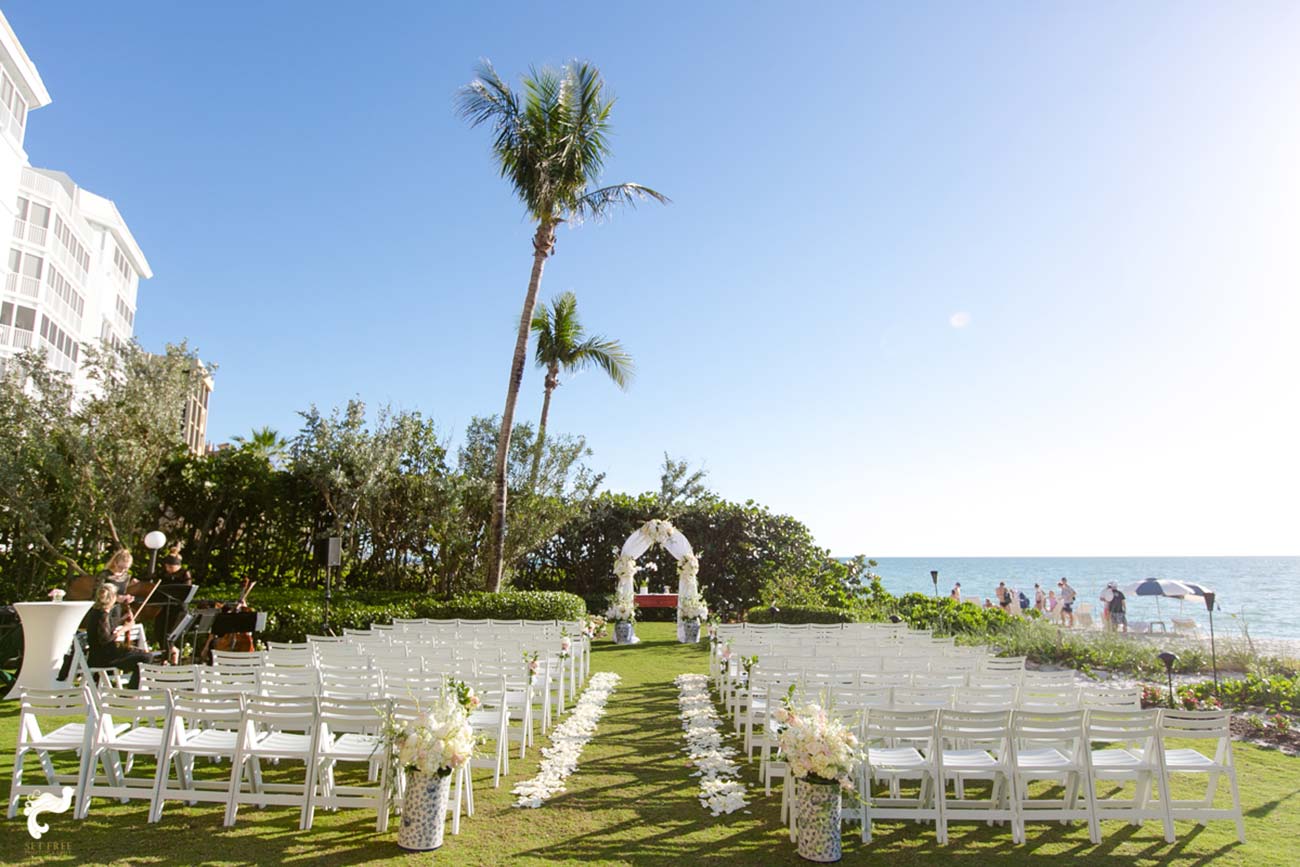 Outdoor wedding ceremony set up by the beach with white petals lining the aisle