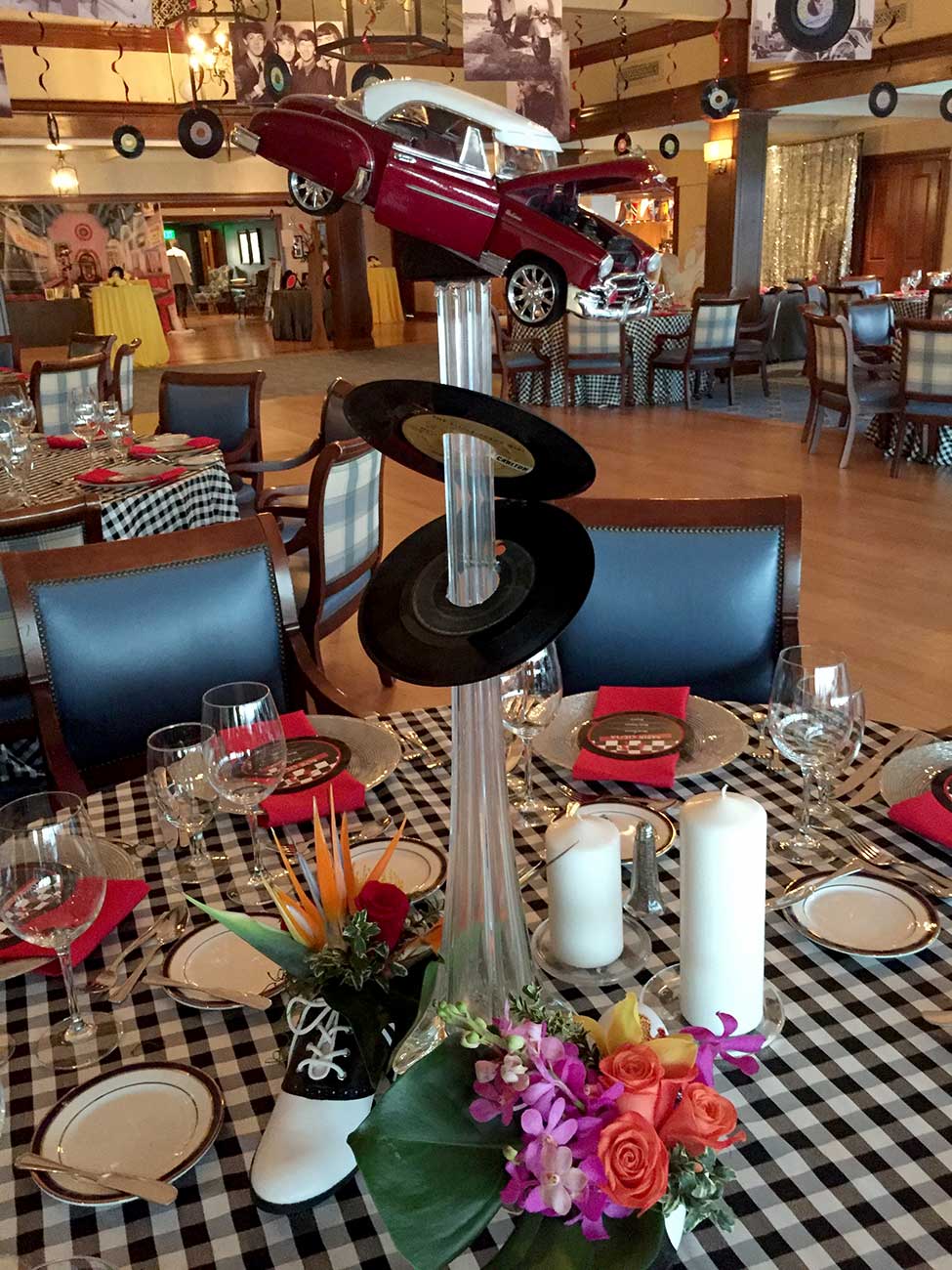 Tabletop decor in a 50's theme with dinnerware, crystal and a 50's car and record floral centerpiece