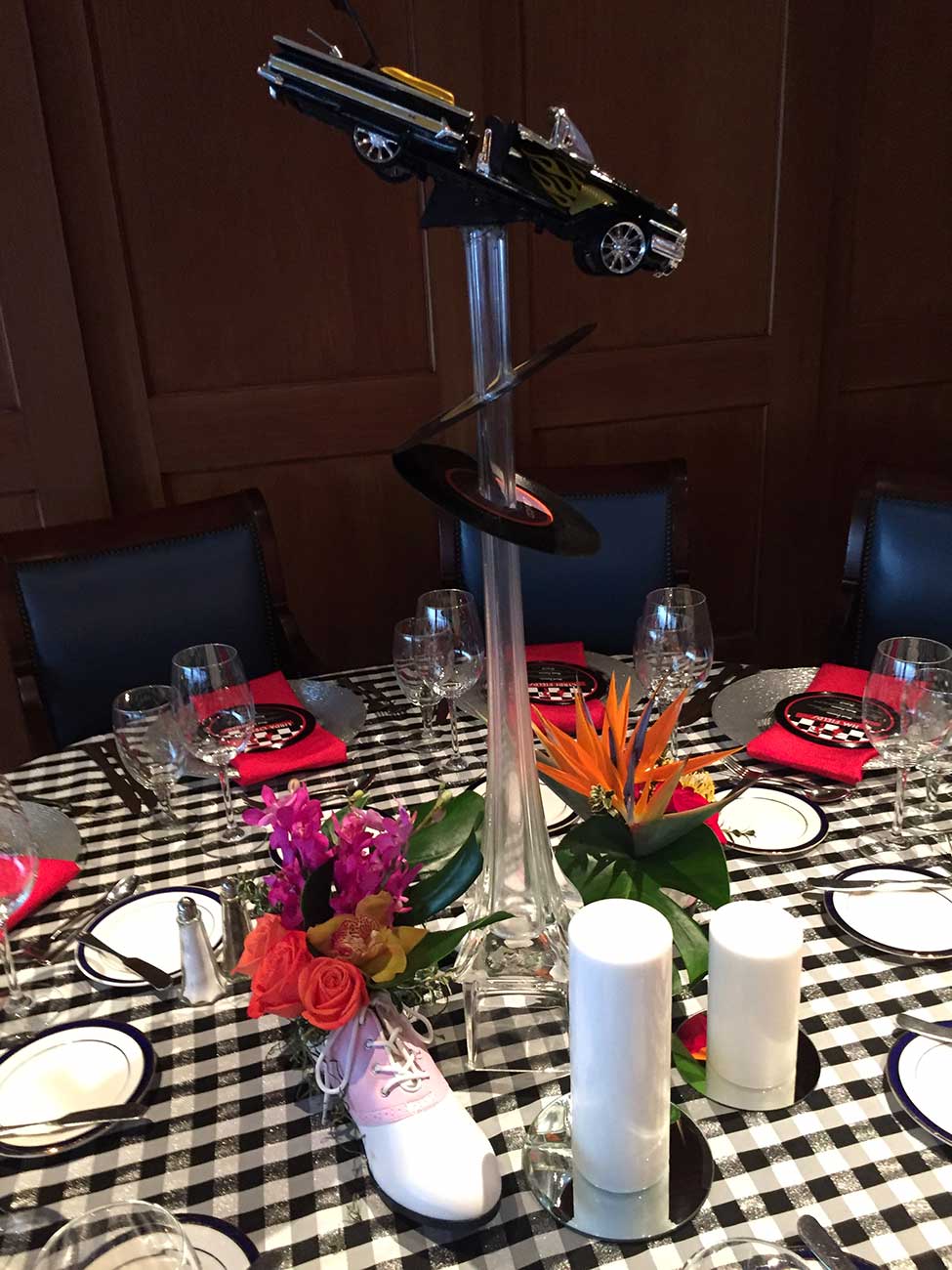 Tabletop decor in a 50's theme with dinnerware, crystal and a 50's car and record floral centerpiece