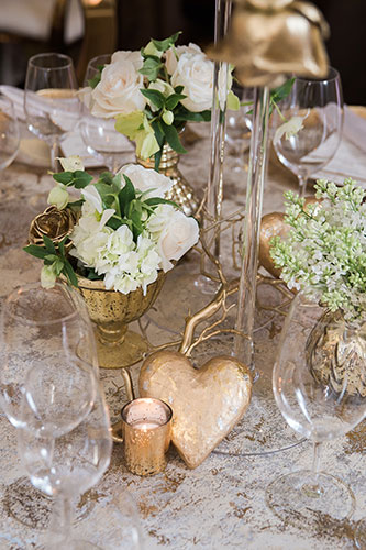 Table top design featuring stemware, silverware, white florals with a gold tone highlight