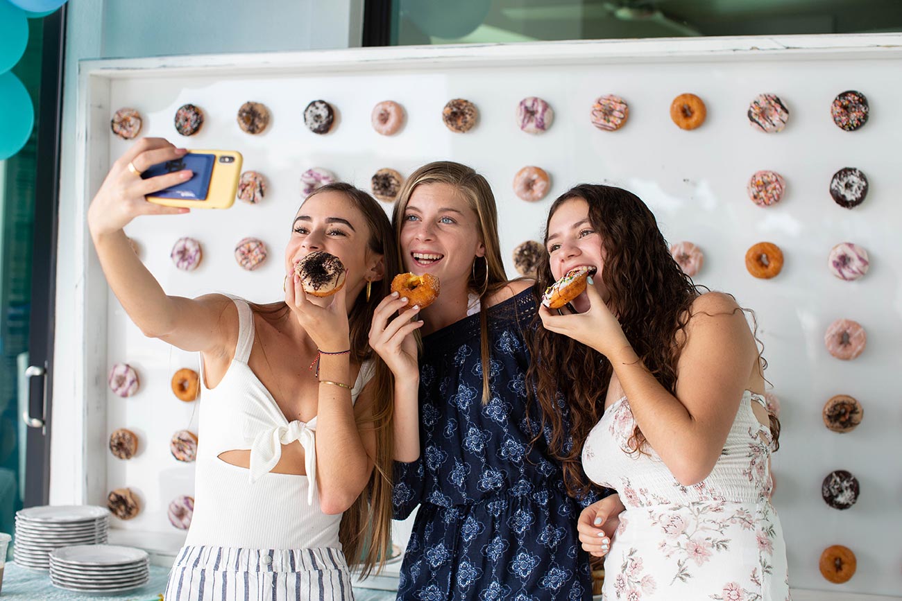 Three teenagers eating doughnuts and smiling while taking a selfie